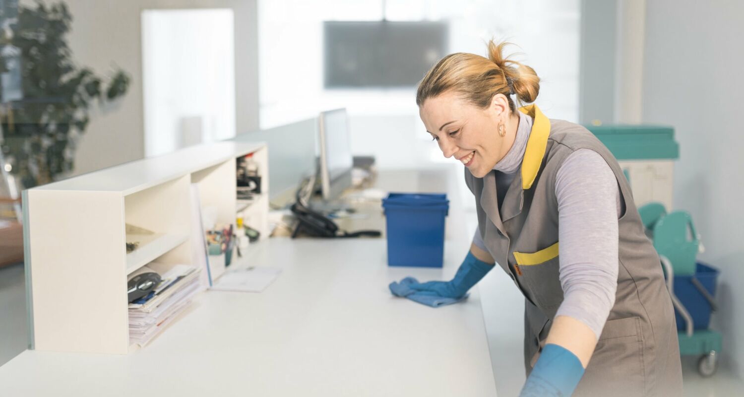 Fachkraft reinigt einen Schreibtisch in einem Büro