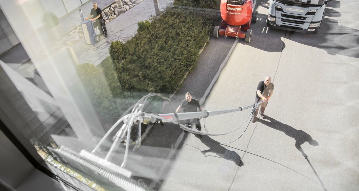 Zwei Arbeiter putzen ein Fenster einer Glasfront über ihnen mit einer ausfahrbaren Bürste