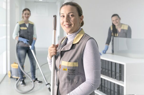 Großaufnahme von Mitarbeiterinnen Drei Mitarbeiterinnen lächeln in die Kamera, wobei die Mitarbeiterin in der Mitte im Vordergrund steht und zwei weitere Damen im Hintergrund.