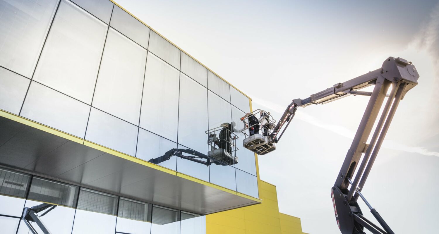 Ein Arbeiter auf einer Hebebühne beim Putzen einer Glasfront