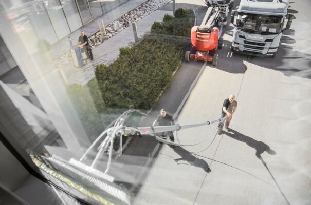 Zwei Arbeiter putzen ein Fenster einer Glasfront über ihnen mit einer ausfahrbaren Bürste