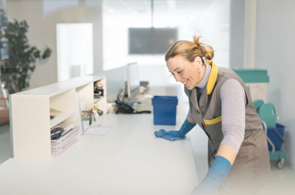 Fachkraft reinigt einen Schreibtisch in einem Büro